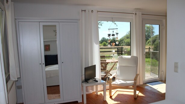 A room with a bed, a desk with a computer, a chair, and a sliding glass door leading to an outdoor area with a table and chairs. - Idyllic "witches house" directly on the lake with private jetty (Hohenferchesar)