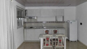 A compact kitchen with a built-in stove, a sink, and a refrigerator. There is a dining table with chairs.