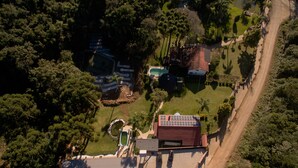 An aerial view of a residential area with a swimming pool, a red-roofed building, and a paved driveway.
