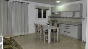 A dining area with a table and chairs, a window with blinds, and a kitchen with cabinets and a sink.