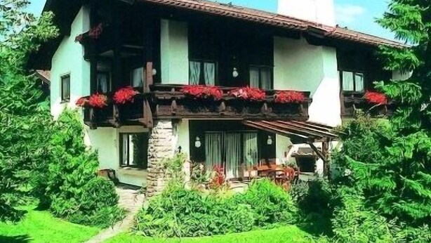 Een twee verdiepingen tellend huis met een stenen gevel, een balkon met rode bloemen en een schoorsteen.