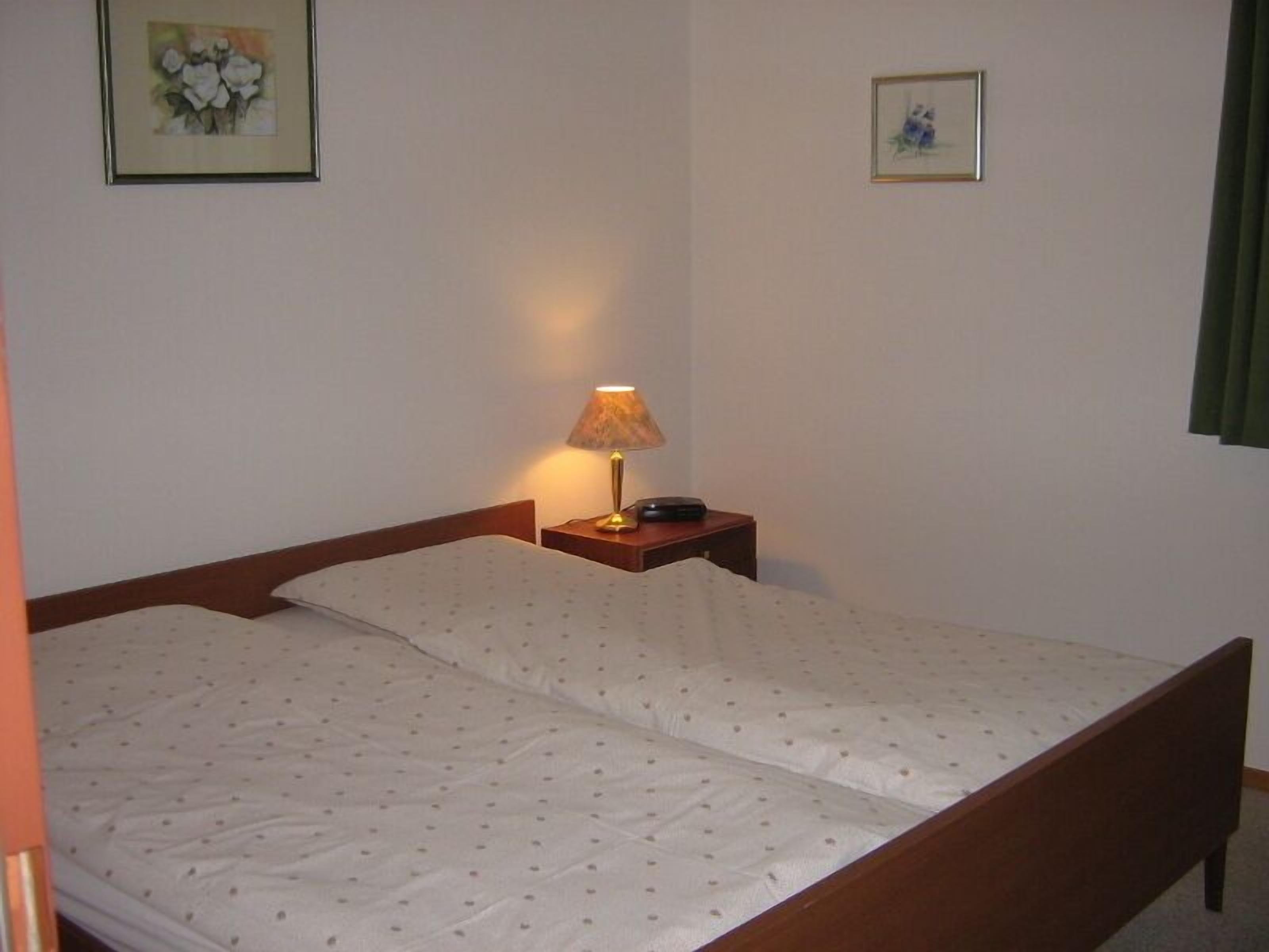 Ein Einzelbett mit Holzrahmen, ein Nachttisch mit Lampe und zwei gerahmte Bilder an der Wand.