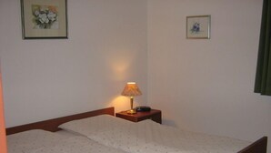 Een enkel bed met houten frame, een nachtkastje met lamp, en twee ingelijste foto's aan de muur.