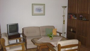 Een woonkamer met een bank, fauteuils, een salontafel, een televisie, een boekenplank en een inlijsting foto aan de muur.