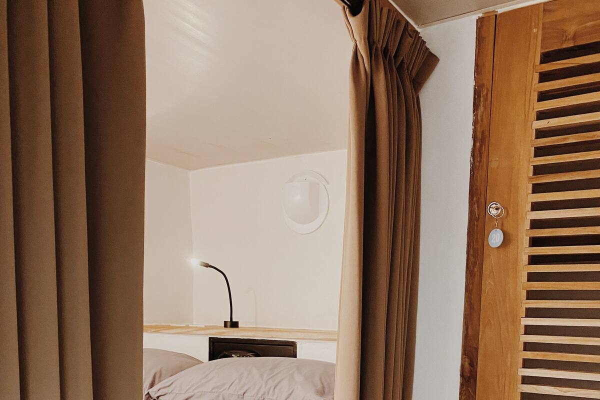 Un dormitorio con cama, mesita de noche, lámpara y puerta de madera con persianas.