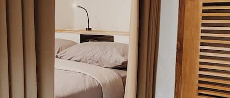 Quarto com cama, mesa de cabeceira, abajur e porta de madeira com venezianas.
