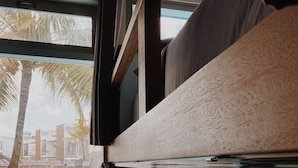 A bunk bed with a window overlooking a pool and palm trees. - Kos One Hostel (Canggu)