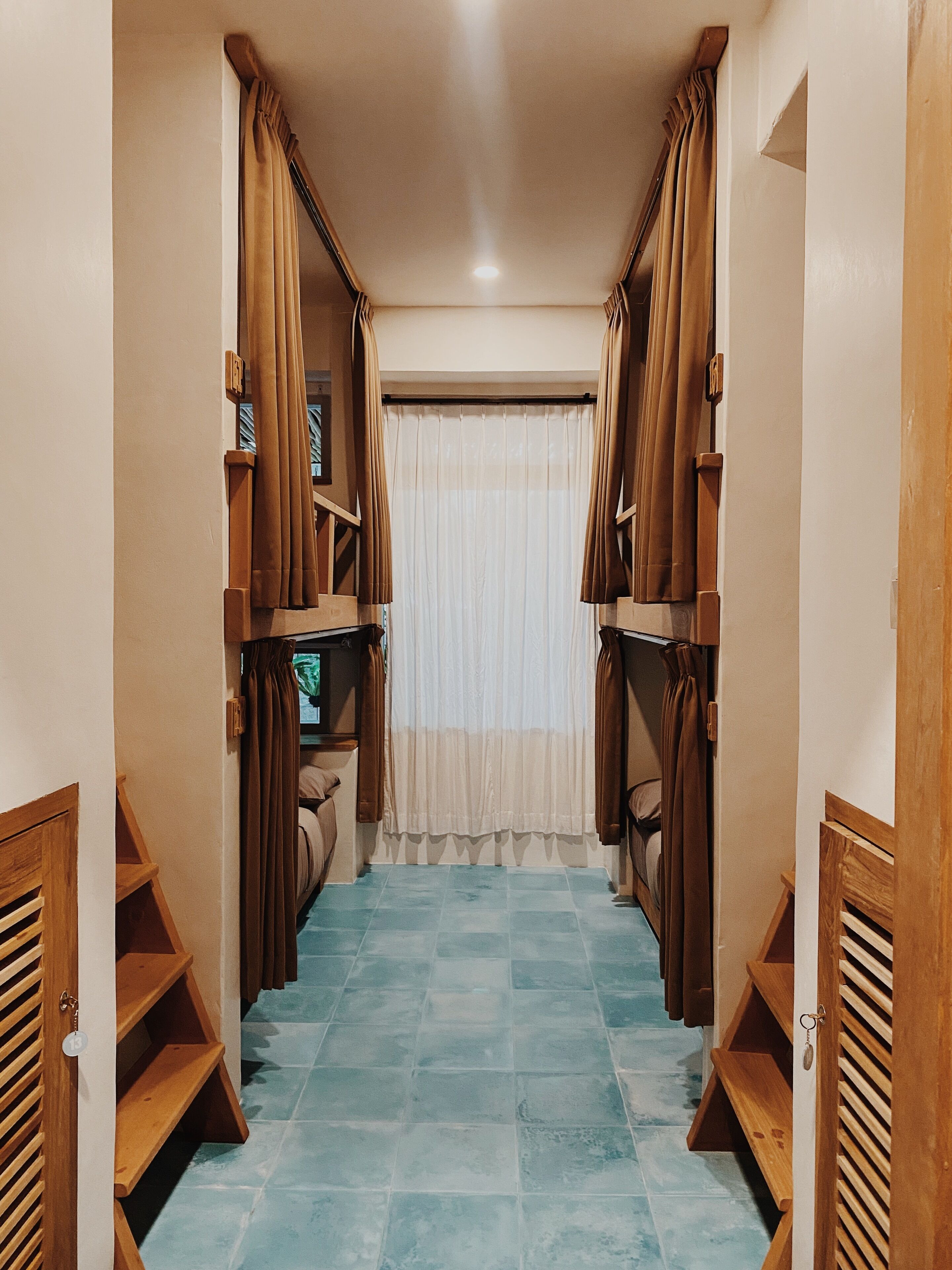A narrow hallway with a blue-tiled floor, wooden shelves on either side, and brown curtains.