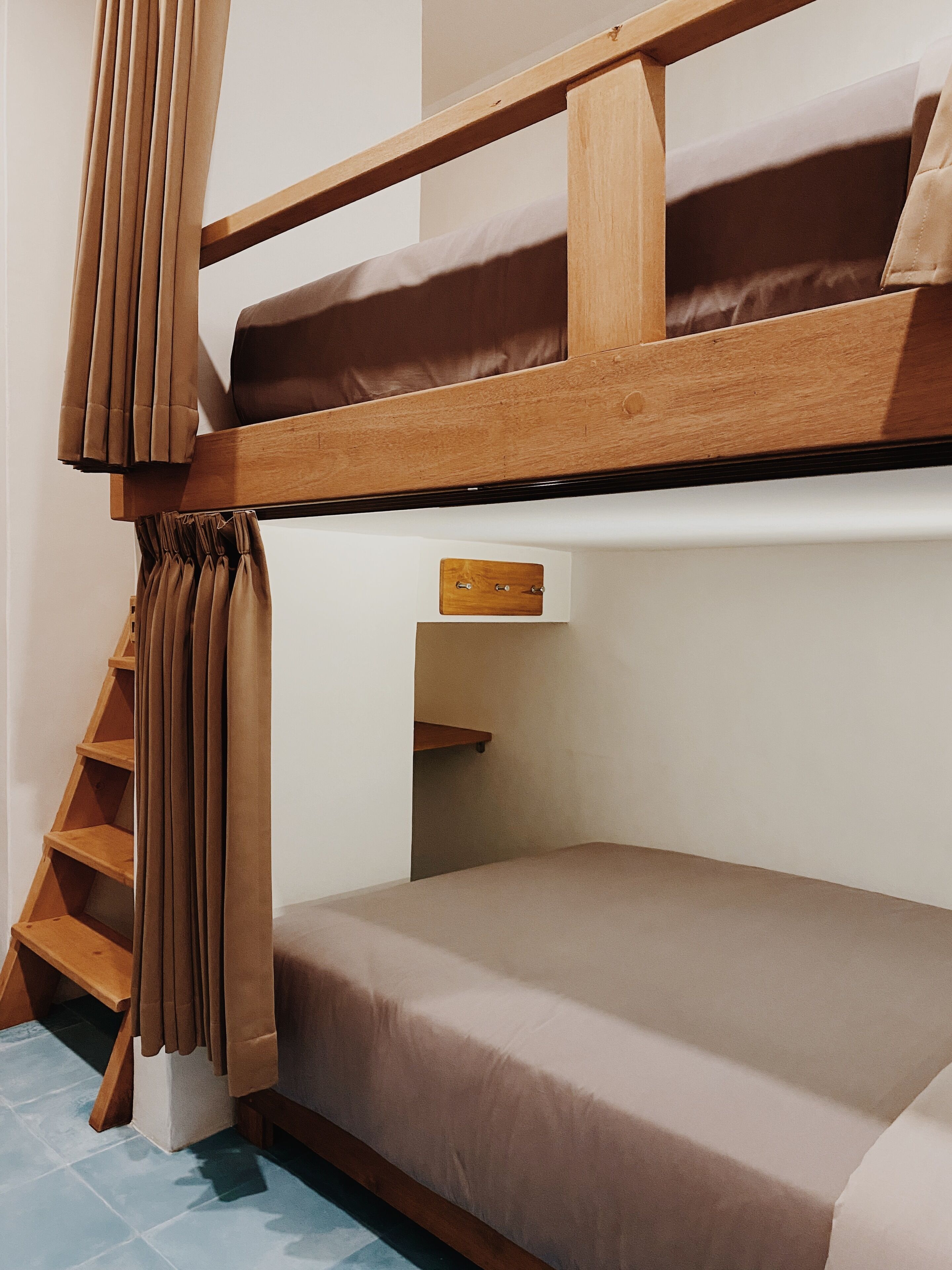 A bunk bed with a wooden ladder, a small shelf, and a curtain.