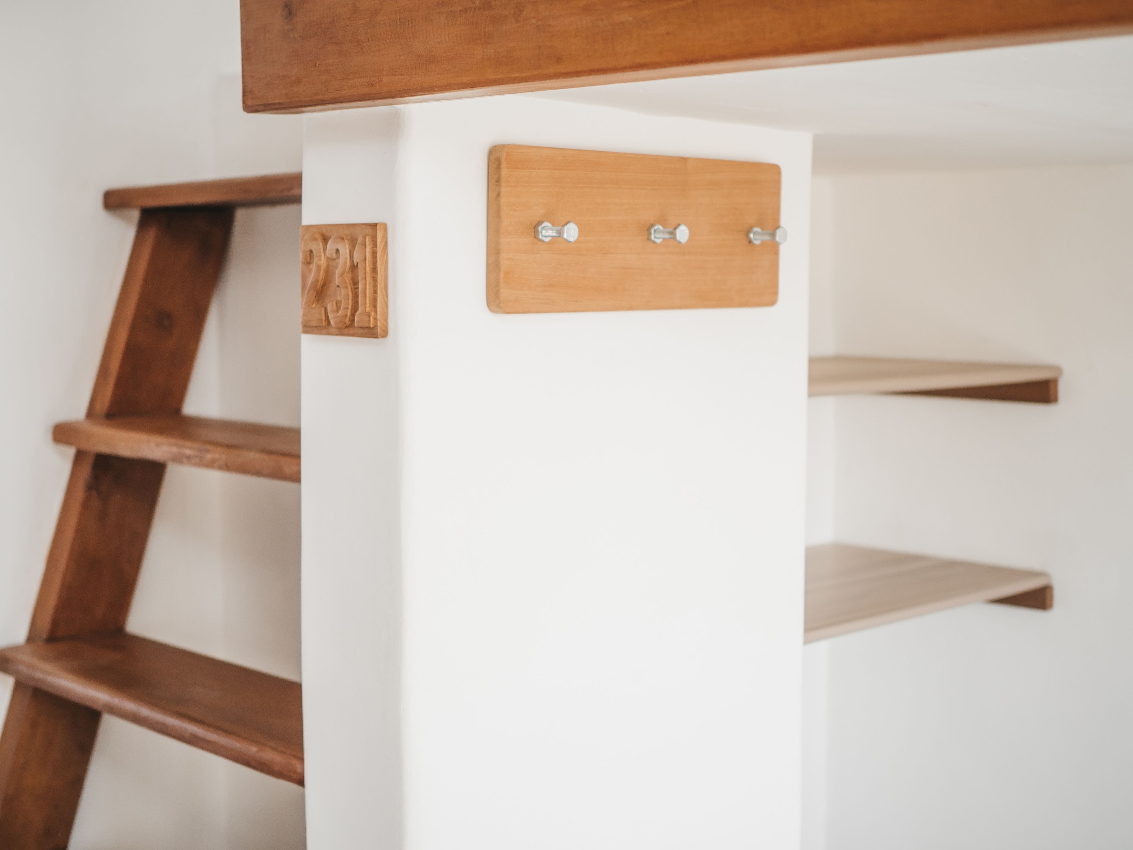Une échelle en bois appuyée contre un mur blanc, avec une étagère en bois et un crochet en métal.