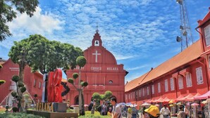 Una iglesia de fachada roja con una cruz en la parte superior, rodeada por una zona de mercado con gente y puestos.