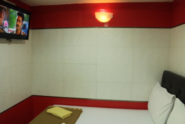 A small, red and white room with a single bed, a television on the wall, and a wall-mounted light fixture. - New Wave Malacca Hotel (Malacca City)