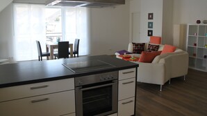 A modern kitchen with a dining area, a sofa, and a bookshelf.