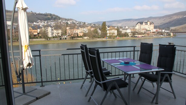 A balcony with a table and chairs overlooking a lake with buildings in the background.