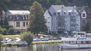 A riverfront view with a boat named 'Moselperle' docked at a pier, surrounded by parked cars and buildings with traditional architecture.