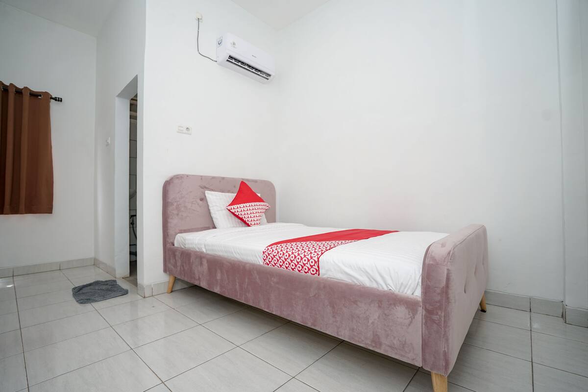 A single-bed room with a pink headboard, white bedding, and a red pillow.