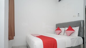 A neatly made bed with a grey headboard, white bedding, and red accents. - OYO 183 The Pipe House (Palembang)