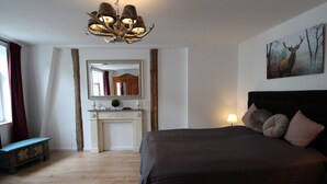 Une chambre à coucher avec un grand lit, un miroir au-dessus d’une cheminée, un lustre et un tableau représentant un cerf accroché au mur.