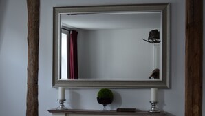 Une pièce avec une cheminée blanche, un grand miroir au-dessus et une poutre en bois sur le côté gauche.