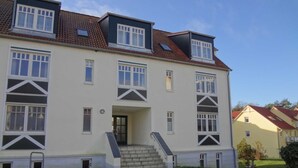 A two-story building with a symmetrical facade, multiple windows, and a central entrance with steps leading to the door. - Family-friendly vacation apartment Seeschwalbe in Koserow - Holiday apartment (Koserow)