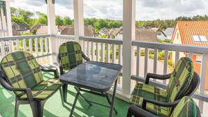 A balcony with a table and chairs, a white railing, and a view of houses and trees. - Family-friendly vacation apartment Seeschwalbe in Koserow - Holiday apartment (Koserow)