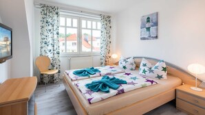 A bedroom with a bed, bedside tables, a chair, a desk, a window with curtains, and a painting on the wall. - Family-friendly vacation apartment Seeschwalbe in Koserow - Holiday apartment (Koserow)