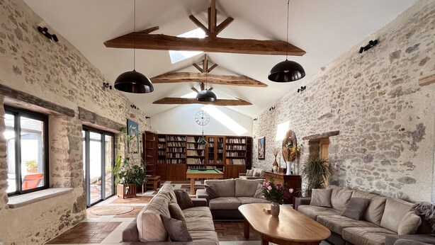 Un salon spacieux avec un plafond haut, des poutres apparentes et une grande collection de bibliothèques.