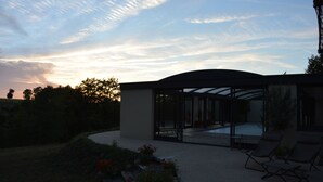 Une maison moderne dotée d’un patio entièrement vitré, d’une piscine et d’un jardin agrémenté de fleurs rouges.
