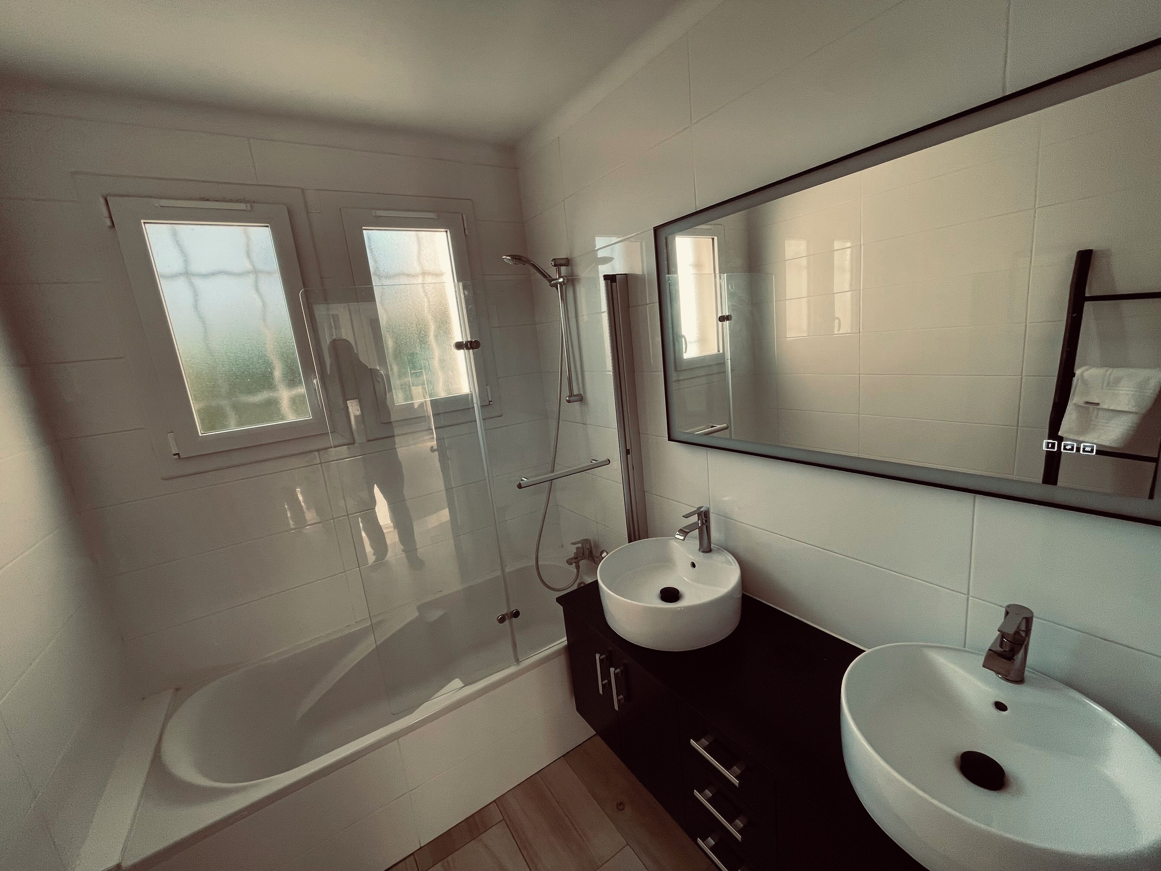 A modern bathroom with a glass-enclosed shower, a white bathtub, and a black vanity with a white sink.
