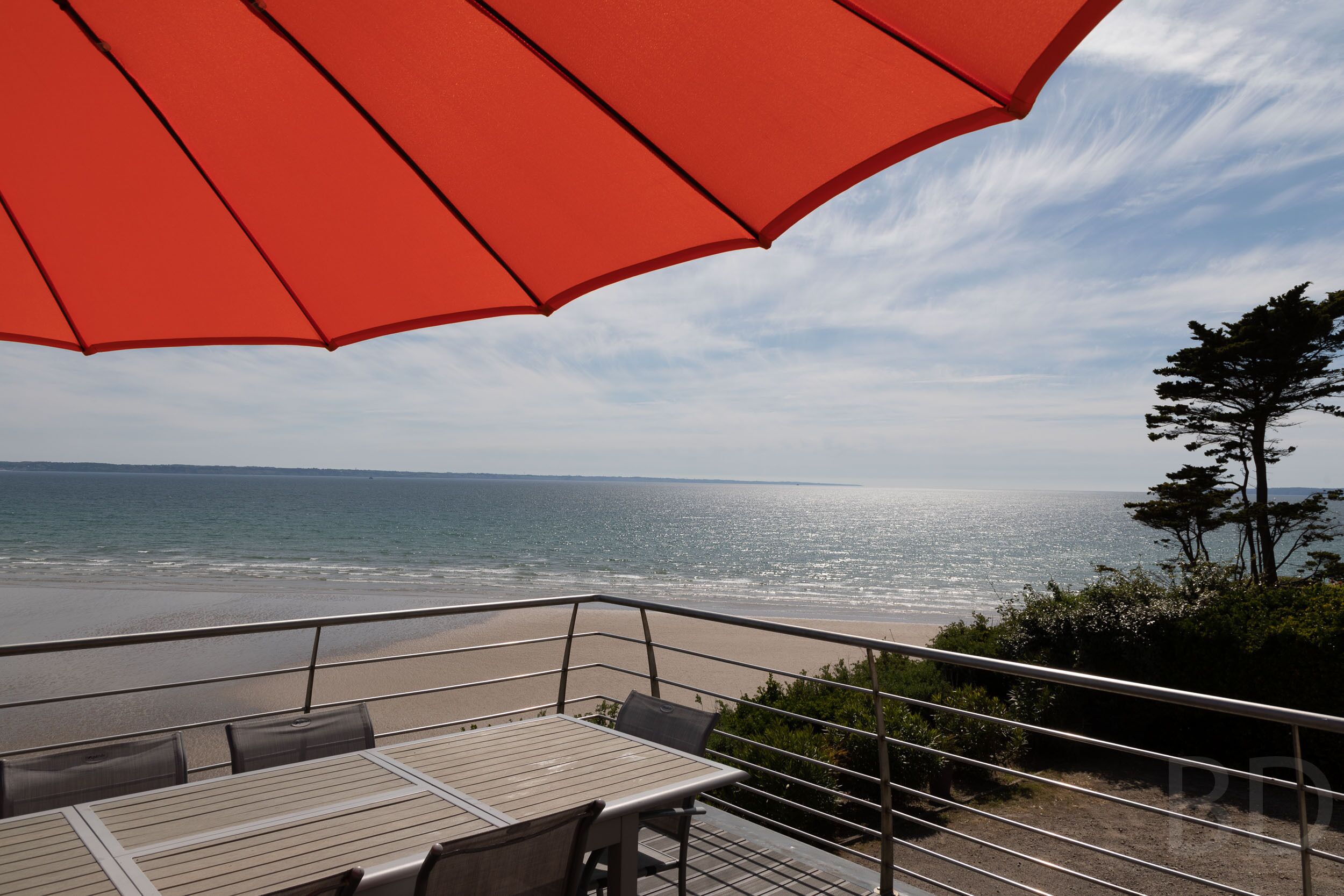 Ein Balkon mit einem roten Sonnenschirm mit Blick auf einen Strand.