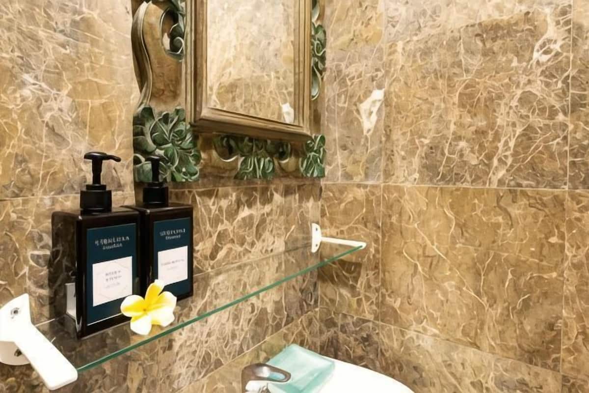 Un baño con paredes de mármol, un estante de vidrio, un grifo blanco y dos botellas negras de champú.