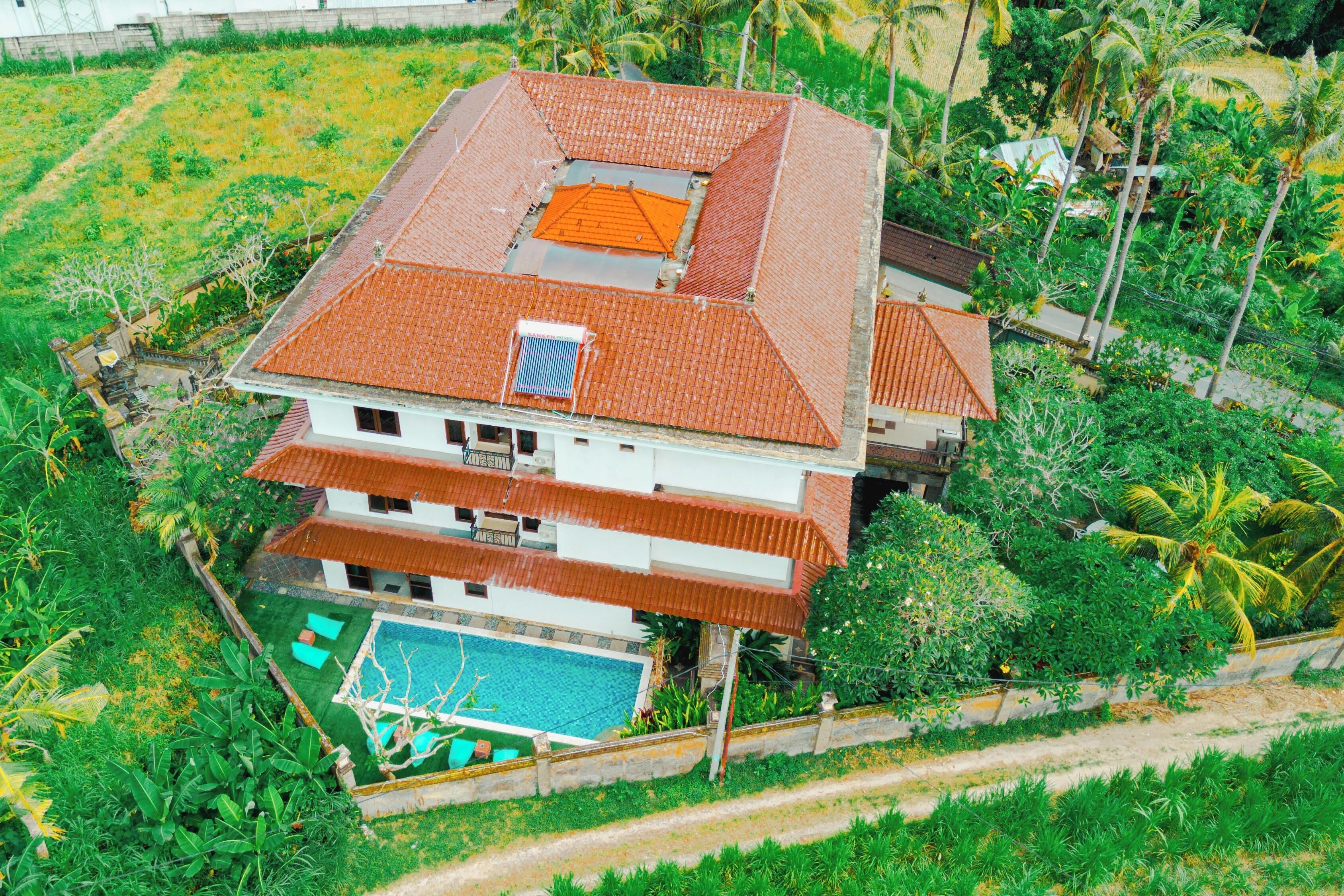 A two-story house with a swimming pool, surrounded by lush greenery and palm trees.