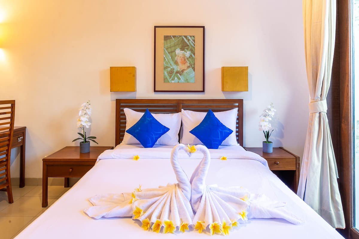 Una habitación de hotel con una cama bien tendida, dos mesitas de noche con lámparas, un cuadro en la pared y una ventana con cortinas.