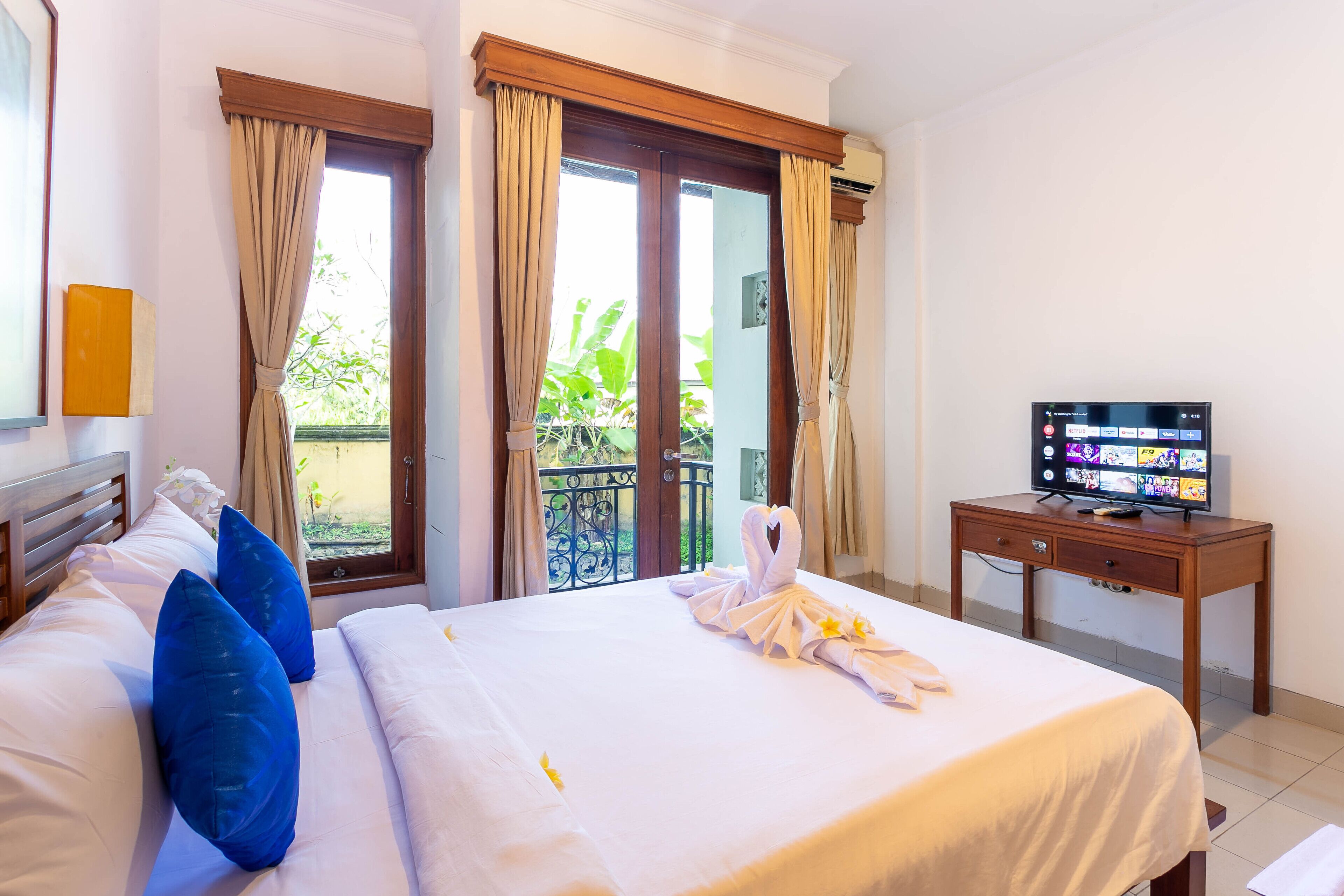 A hotel room with a bed, a TV, and a balcony with curtains.