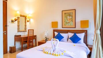 Quarto de hotel com cama bem arrumada, uma escrivaninha com cadeira, uma mesinha com planta e um quadro na parede.