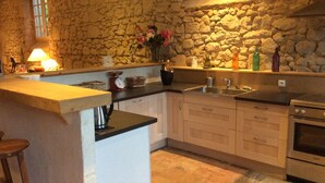 Una cocina con pared de piedra, armarios de madera, un lavamanos y una estufa.