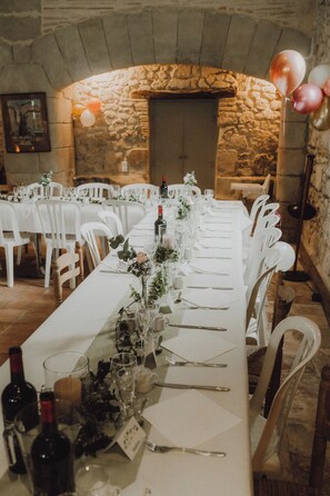 A long dining table set for a formal event, with chairs on both sides, in a room with stone walls and a fireplace. - Cottage character, spacious volumes, warm and serene. (Tombebœuf)