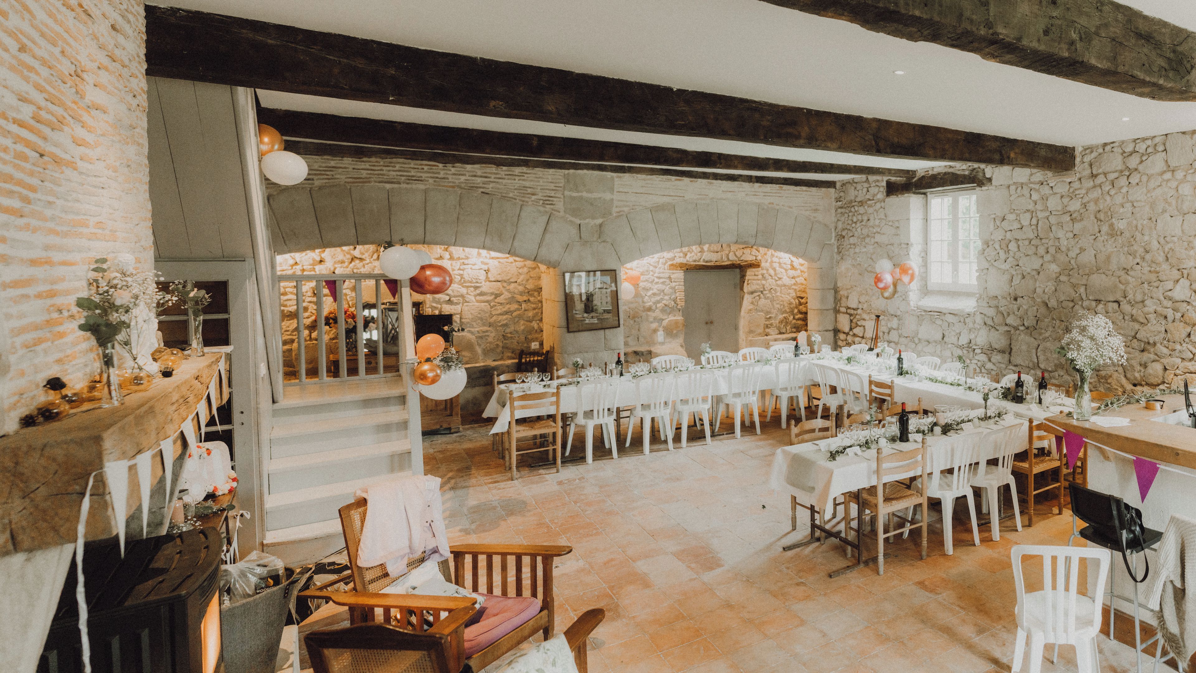 Une vaste salle aux murs de pierre, dotée de nombreuses tables dressées pour le repas et d’un plafond en bois rustique.