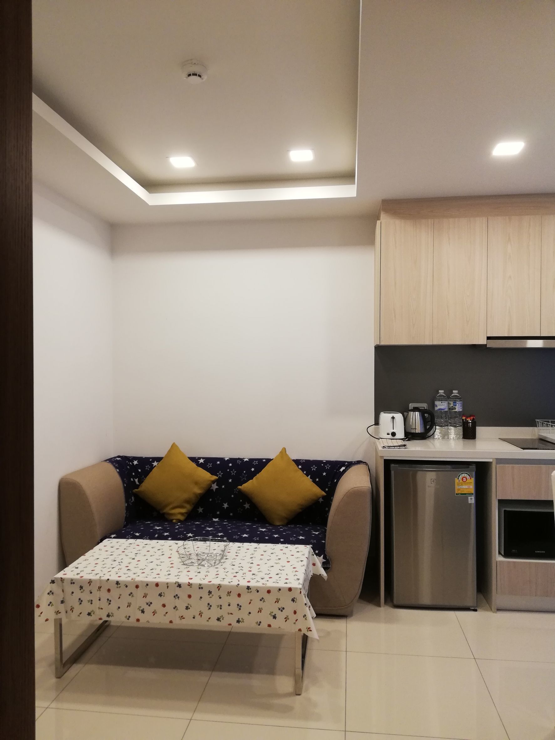 Ett kompakt bostadsutrymme med en soffa, ett litet bord, en liten köksdel och en taklampa.