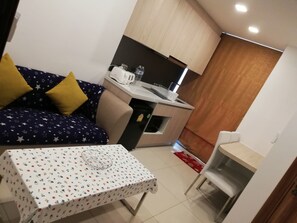 Un espace de vie compact comprenant un coin cuisine, un canapé recouvert d’un tissu à motifs étoilés, une petite table à manger et une chaise.