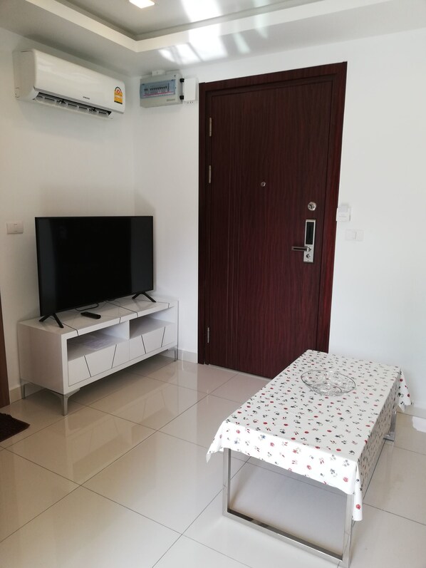 A room with a TV on a white cabinet, a wooden door, and a table with a floral tablecloth.
