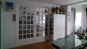 Un comedor con una mesa de vidrio, armarios blancos y vista a otra habitación.