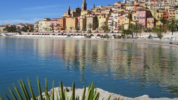 Un paisaje urbano costero con una destacada torre de iglesia, un puente y un paseo marítimo.