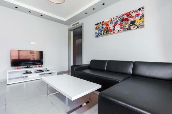 A modern living room with a black leather sofa, a white coffee table, a flat-screen TV on a white entertainment unit, and a colorful abstract painting on the wall. - Superb Apartment in full Marrakech, Province of Marrakech, Morocco Gueliz (marrakech)