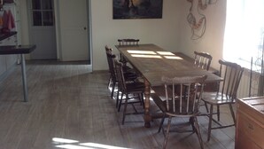 Ein Essbereich mit einem langen Holztisch, Stühlen, Pendelleuchten und einem Gemälde an der Wand.