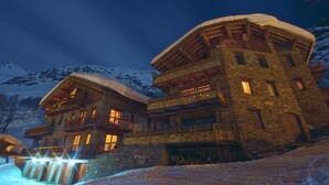 Un bâtiment en pierre doté de nombreux balcons et dont le toit est recouvert de neige, le tout entouré de montagnes.