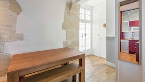 A room with a wooden table, a stone wall, and a view of a kitchen with red cabinets. - Suit Du Lion/AC Historic Flat, Marais, 4-5 Guests (Paris)