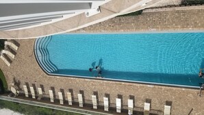 An aerial view of a swimming pool with a tiled deck, lounge chairs, and a brick wall.