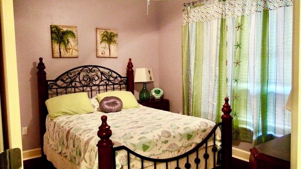 A bedroom with a bed, a nightstand, a lamp, and a window with curtains.