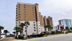 A multi-story hotel with a beige facade, multiple balconies, and palm trees in the foreground.